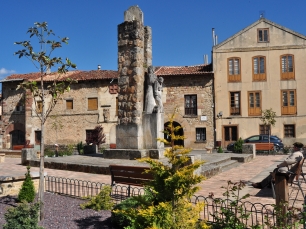 Una plaza del casco urbano de Cervera de Pisuerga, con edificios y un monumento de piedra; el paisaje construido de la villa sirve de contrapunto al santuario medieval excavado en un afloramiento.