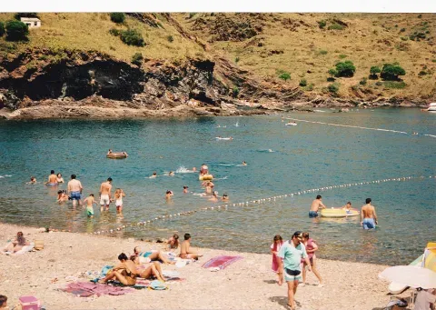 Una playa de El Port de la Selva en una fotografía de verano. La escena sitúa el litoral donde las canteras de gneis dejaron una huella en la costa.
