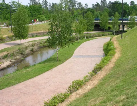 El paseo acompaña al cauce y mantiene una franja abierta entre la corriente, la vegetación y las nuevas áreas urbanas de Bertamiráns.