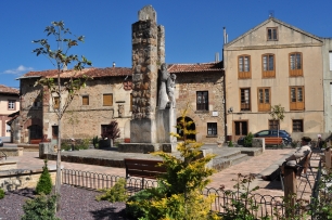 Una plaza del casco urbano de Cervera de Pisuerga, con edificios y un monumento de piedra; el paisaje construido de la villa sirve de contrapunto al santuario medieval excavado en un afloramiento.